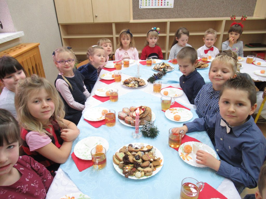 Wigilijka w grupie dzieci 4-5 letnich. dzieci siedzą przy świątecznych stołach w swojej sali. znajdują sie na nich słodkie ciasteczka.