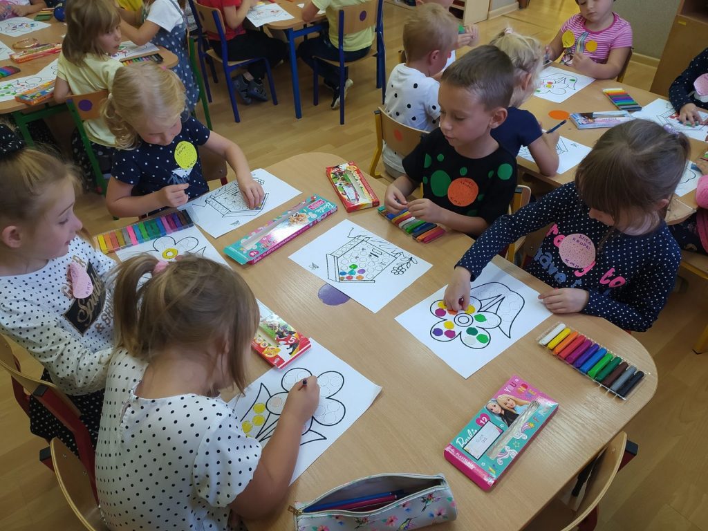 Dzieci siedzą przy stoliku. Na stoliku znajdują się obrazki: kwiatka lub ula.Kropeczkami z kolorowej plasteliny wyklejają obrazki. 