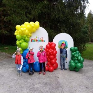 [rzedszkolaki stoją przed ścianką zrobioną z duchanych, kolorowych balonów. balonów
