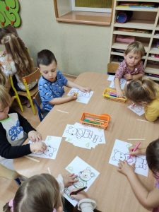 Dzieci siedzą przy stolikach i kolorują wiślańskie misie