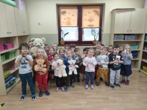 Dzieci stoją w półkolu w trzech rzędach. Trzymają w rękach pluszowe misie.