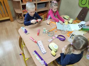 Dzieci siedzą za stolikami, wykonują dziurkaczem ozdoby na zakładkę. 