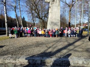 Przedszkolaki stoją pod pomnikiem i śpiewają hymn