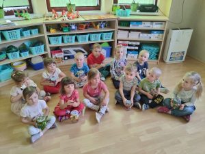 Dzieci siedzą w dwóch rzędach w półkolu przed każdym stoi udekorowany słoik 