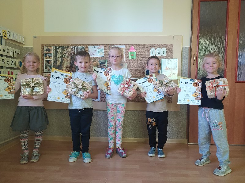 Na zdjęciu dzieci nagrodzone w konkursie . W rękach trzymają dyplomy,książeczki i nagrodę w postaci miodu