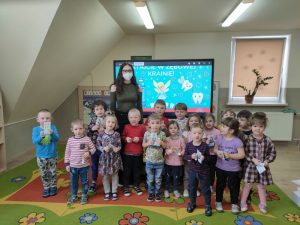 Dzieci stoją w dwóch rzędach na środku sali razem z panią stomatolog.