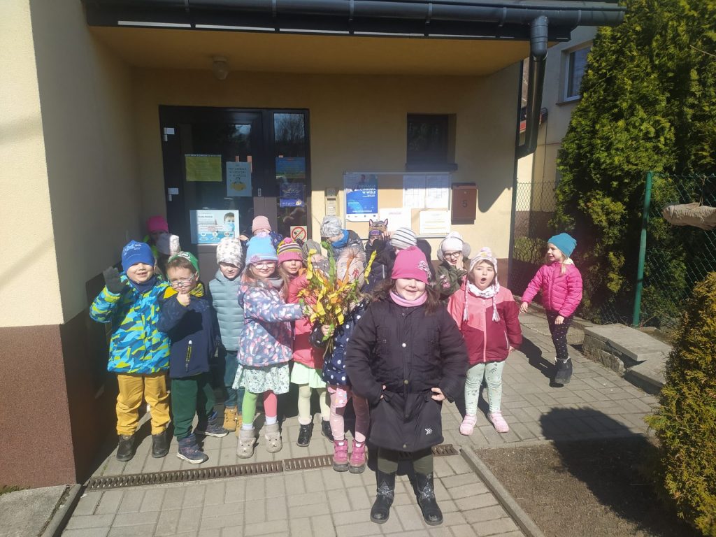 Dzieci ustawione w 2 rzędach przed budynkiem przedszkola , Jedno dziecko trzyma ustrojony w kolorowe bibułki gaik . 