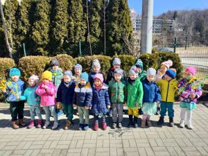 Dzieci stoją w ogródku przedszkolnym, śpiewają piosenkę o wiośnie.