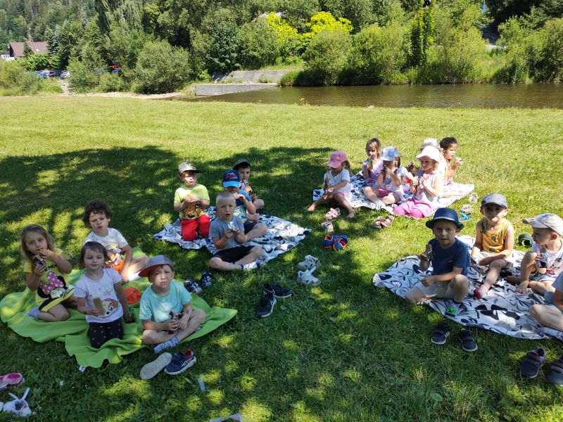 Dzieci siedzą na kocach, piją soczki i jedzą ciasteczka.