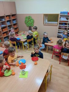 dzieci siedzą przy stolikach w sali, jedzą jabłka, piją samodzielnien przygotowany sok z marchewki jedzą jabłka i piją