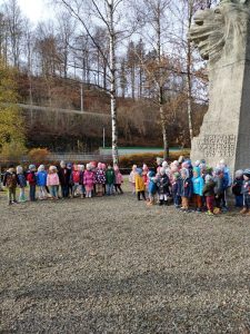Dzieci stoją pod pomnikiem w grupach.
