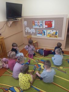 Dzieci siedzą na dywanie oglądają historyjkę z Elemelkiem.