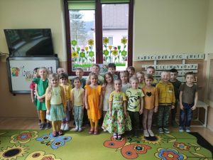 Dzieci stoją w 3 rzędach ubrani na żółto zielono,