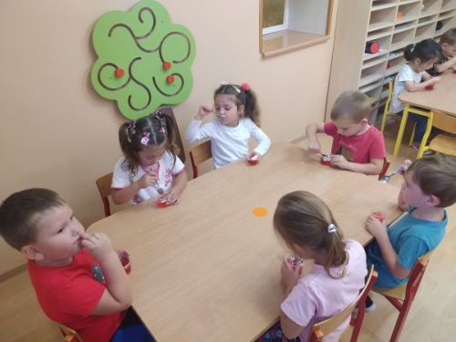 Dzieci siedzą przy stoliku i jedzą czerwoną galaretkę z bitą śmietaną