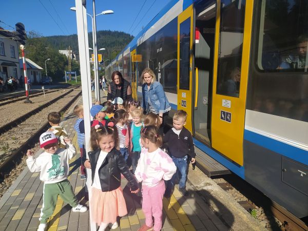 Dzieci stoją na peronie przed pociągiem wraz z opiekunami