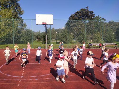 Dzieci w rozsypce na boisku sportowym biegną przez boisko w wyznaczonym kierunku.