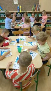 dzieci siedząprzy stolikach i malują herb Wisły, na stolikach farby, pędzle, i prawie gotowe prace
