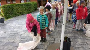 Dzieci stoją w kolejce, pierwsze dziecko zakłada worek