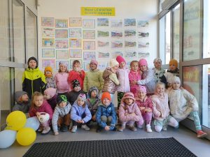 Grupa dzieci z zerówki pozują do zdjęcia, ustawione w dwóch rzędach, w tle rysunki dzieci TV