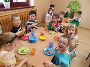 Dzieci siedzą przy stoliku i jedzą karnawałowe smakolyki
