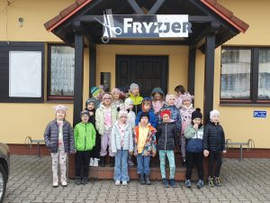 Grupa ,,Zerówka" stoi przed budynkiem, w tle napi Fryzjer