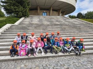 dzieci przed planetarium, Grupa średniaki w pomarańczowych czapkach siedzą na schodami przed budynkiem Planetarium 