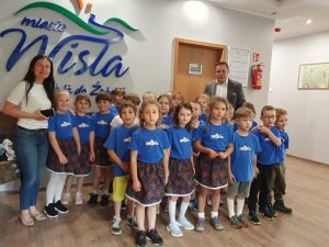 Dzieci pozują do zdjęcia na tle loga Wisły, ubrane dziewczynki w niebieskie koszulki i niebieskie spódnice w kwiaty