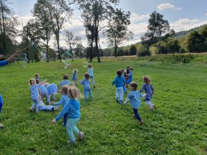 Dzieci w niebieskich ubrankach biegają po łące 