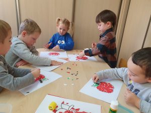 Dzieci siedzą przy stoliku wyklejaja kontury różnych przedmiotów papierem kolorowym