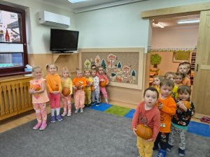 Maluchy ustawione w dwóch rzędach, dzieci trzymają dynie,