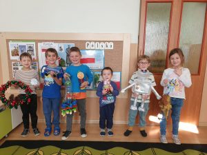 Dzieci ustawione trzymają wykonane prace z wtórnych materiałów: robot. wieniec adwentowy, pracę z butelek plastikowych