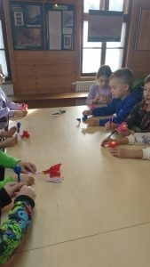 Dzieci siedzą przy stole i wykonują kwiatki z bibułki.