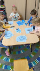 Dzieci rysują chmury deszczowe na niebieskiej kartce kredkami