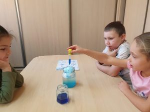 Dzieci siedzą przy stoliku i wykonują doświadczenia z wodą 