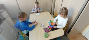 Dzieci siedzą przy stoliku  i utrwalają kształty, oraz 