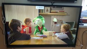 Postać detektywa Łodygi na ekranie i dzieci. Postacie siedzą przy stole.