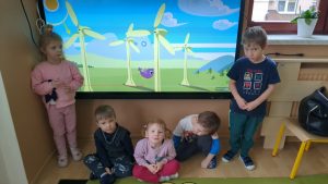 Czworo dzieci stoi przed plansz, na której są wiatraki wytwarzające prąd 