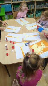 Dzieci siedzą przy stoliku i wykonują pracę plastyczną z papieru, wiatrak.