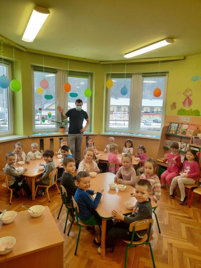 Na zdjęciu znajduje się pan kucharz i dzieci siedzące przy stolikach, które jedzą lody.