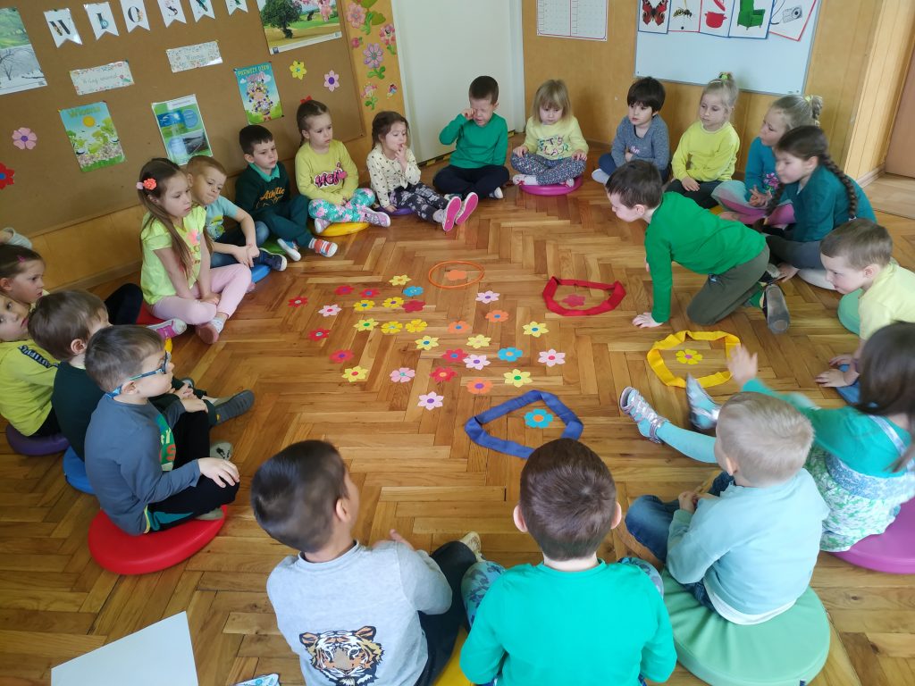Dzieci siedzą w kółku i układają kolorowe kwiatki.